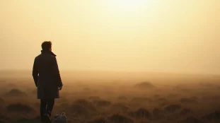 Silhouette solitaire contemplant un ciel d'aube brumeuse au bord d'une lande, illustration de la religion naturelle comme intuition du divin dans le paysage